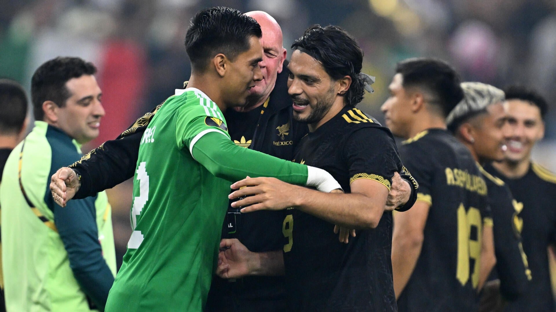 Soccer players in black and green Mexico jerseys embrace and smile together on a field following a match.