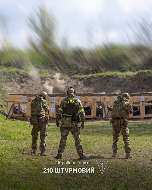Three soldiers in camouflage uniforms stand at a firing range facing wooden target frames marked with numbers and tires, with a watermark reading "210polk.mil.gov.ua."