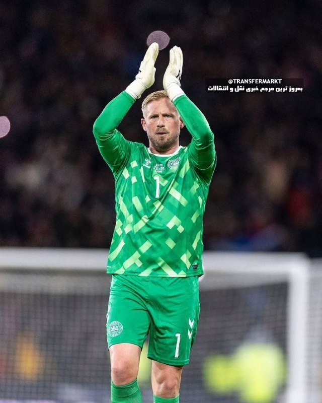 A bearded goalkeeper in a green patterned jersey with the number 1 applauds with gloved hands raised, standing in front of a goal net.