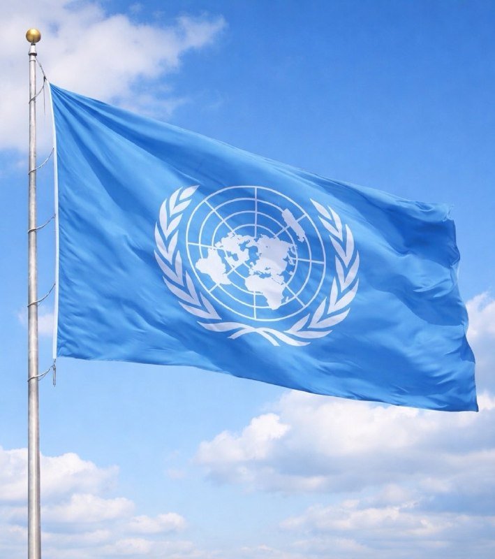 The light blue United Nations flag, featuring a white world map encircled by olive branches, waves on a silver flagpole against a partly cloudy sky.