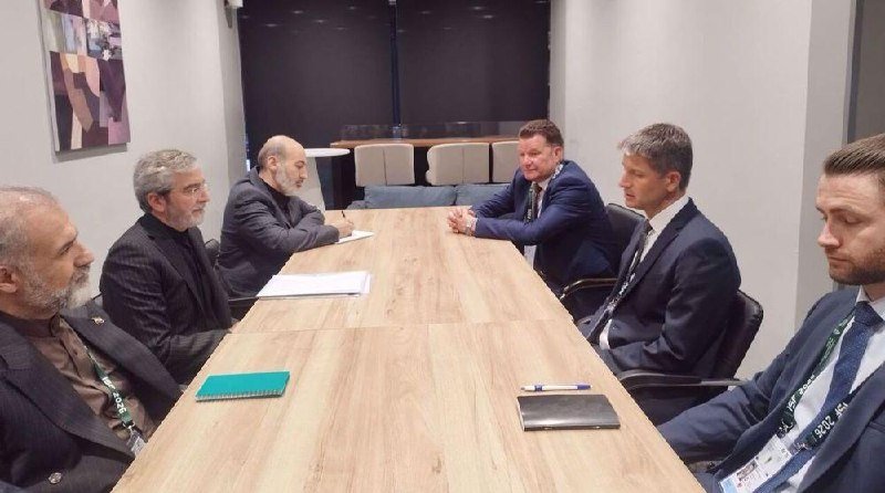 Six men in suits sit around a wooden conference table in a meeting room, with notebooks and pens visible on the table.