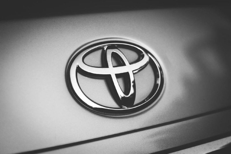 Black-and-white close-up of a chrome Toyota emblem mounted on a vehicle's body panel.