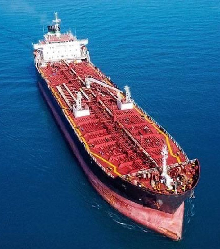 Aerial view of a large red and black oil tanker with a white superstructure sailing on calm blue water.