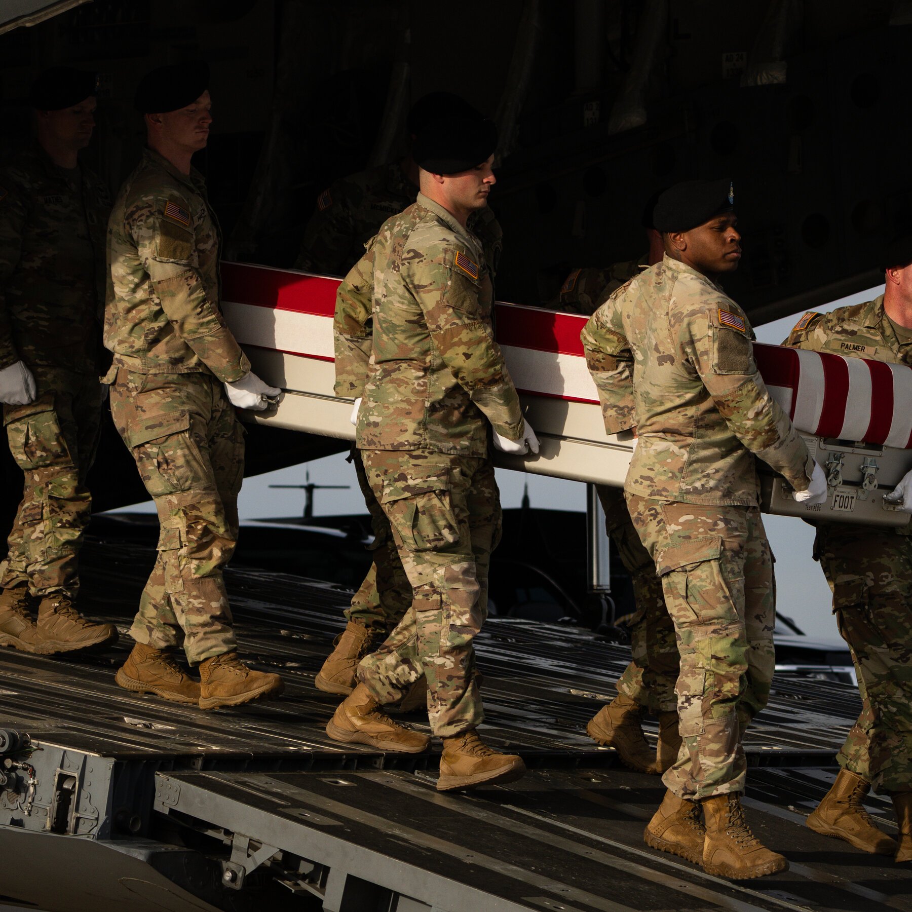 Soldiers in camouflage uniforms carry a flag-draped transfer case off a military aircraft.