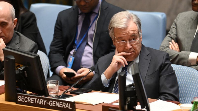 A gray-haired man in a suit sits at a desk labeled "SECRETARY-GENERAL," resting his chin on his hand during what appears to be a formal council meeting.