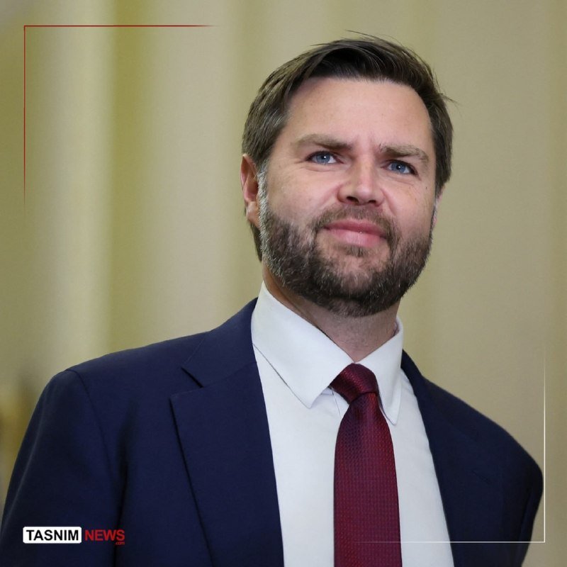 A bearded man in a dark suit, white shirt, and maroon tie looks off-camera against a plain beige background, with a "TASNIM NEWS" watermark visible.