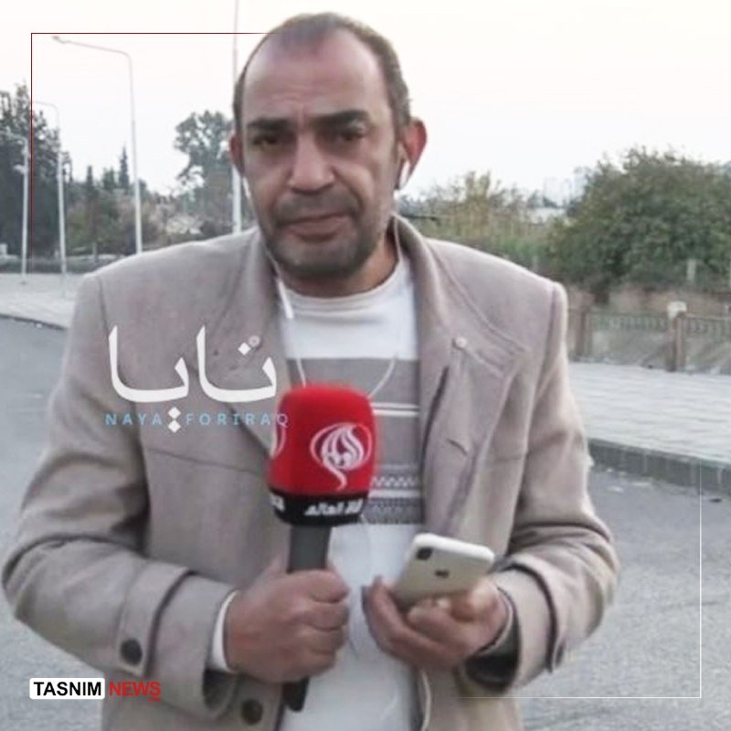 A man in a beige jacket speaks into a red Al Mayadeen microphone while holding a smartphone on a street, with Naya For Iraq and Tasnim News logos visible.
