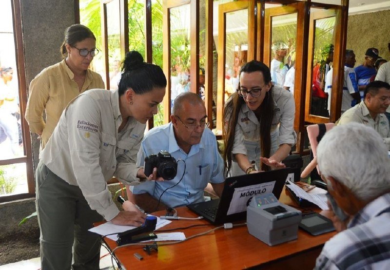 Several people gather around a table with a laptop labeled "MÓDULO," where a woman points to the screen while another holds a camera.