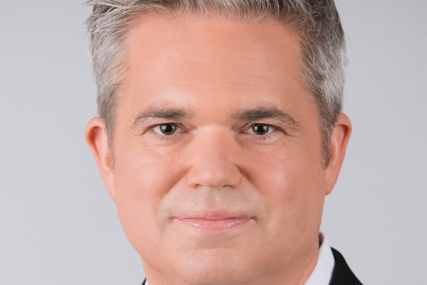 A close-up portrait shows a man with short silver hair against a plain light-colored background.