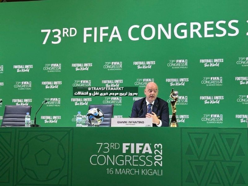 A bald man in a suit speaks at a press conference table bearing a "Gianni Infantino" nameplate, with a football and golden trophy in front of a green "73rd FIFA Congress" backdrop.