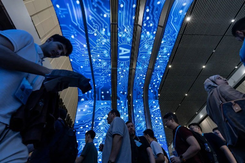 Attendees walk beneath a large blue digital display featuring circuit-board patterns and an "AI" logo at what appears to be a technology conference or exhibition.