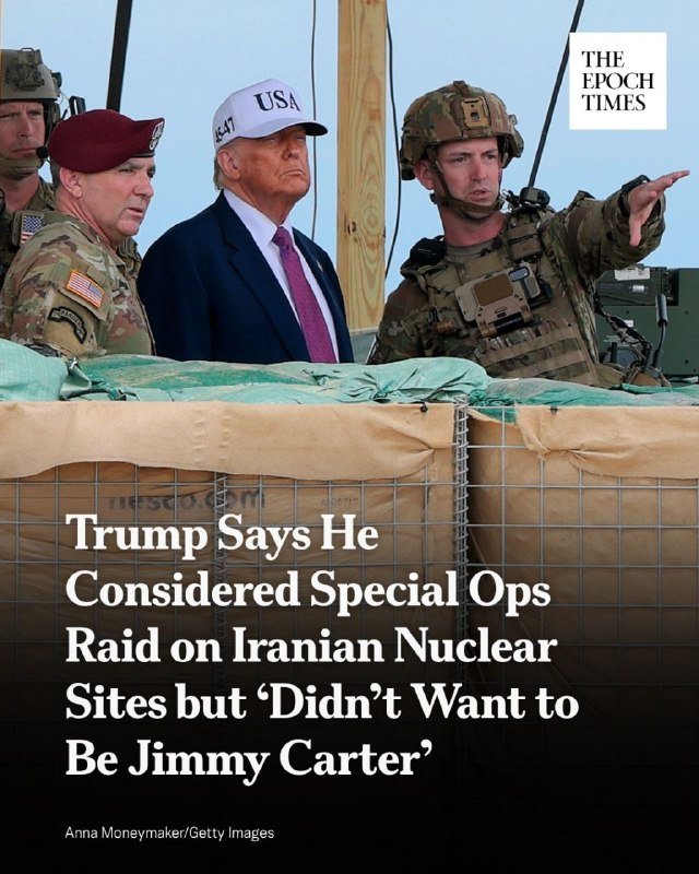 A man in a suit and "USA" cap stands alongside military personnel, including a soldier pointing into the distance, in front of stacked sandbags.