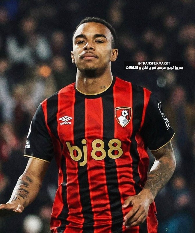 A footballer in a red and black striped AFC Bournemouth jersey with "bj88" sponsor and Umbro logo stands on the pitch with a blurred crowd behind him.