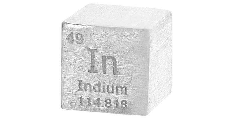A silver-colored metallic cube engraved with "In," "Indium," "49," and "114.818" rests against a white background.