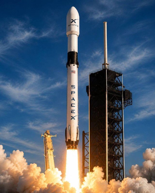 A white SpaceX rocket marked "SpaceX" lifts off from a launch pad, with flames and billowing smoke beneath it against a partly cloudy blue sky.