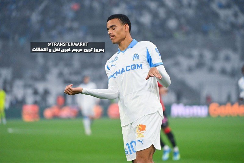 A soccer player in a white Olympique de Marseille jersey with "CMA CGM" sponsorship celebrates on the field during a rainy match, with blurred stadium seating in the background.