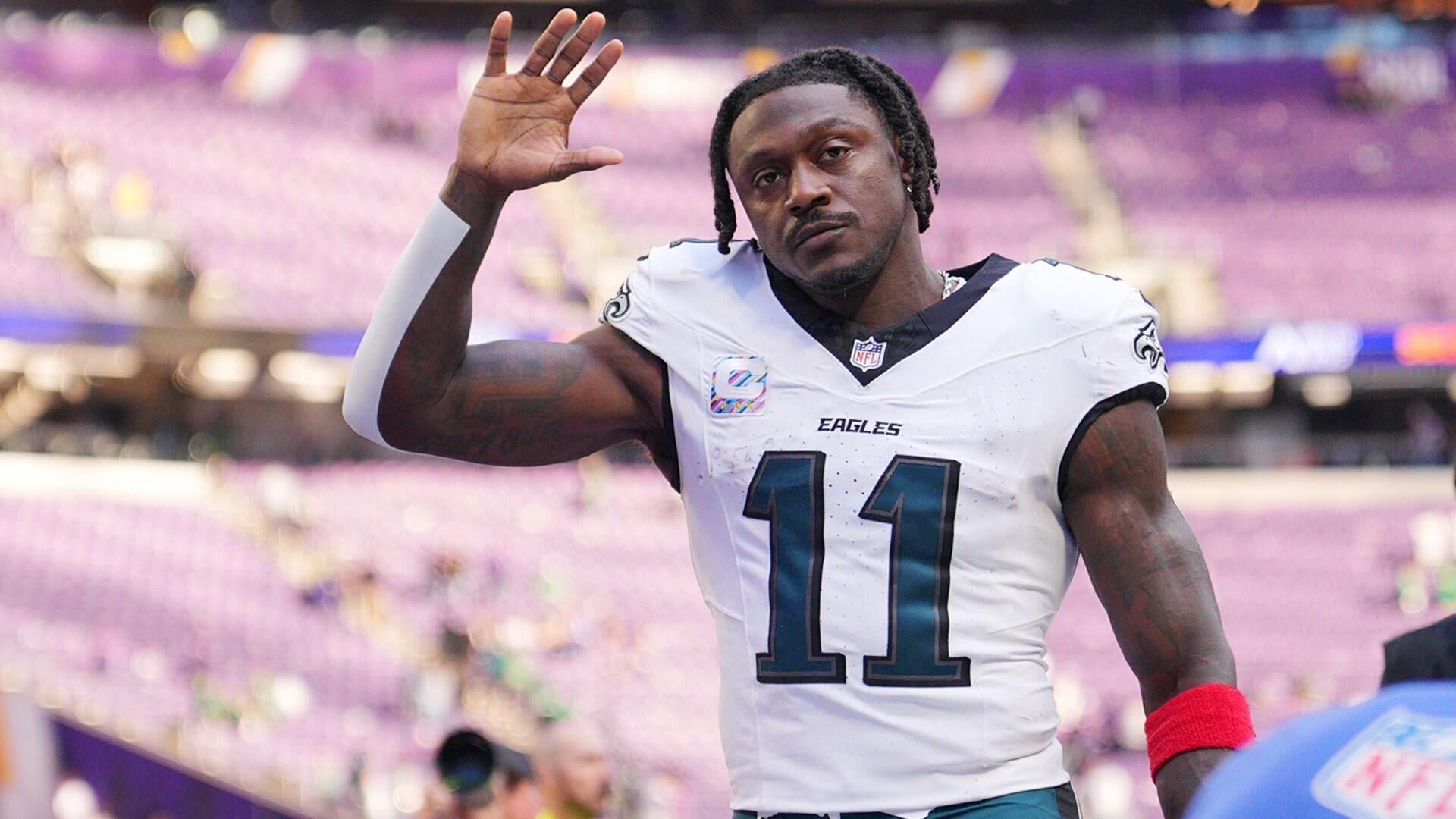 A football player wearing a white Eagles jersey with the number 11 waves to fans in a stadium filled with purple seats.