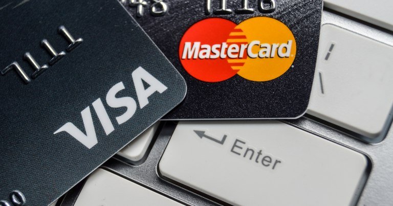 Two credit cards, displaying the Visa and MasterCard logos, rest on a silver computer keyboard above the Enter key.