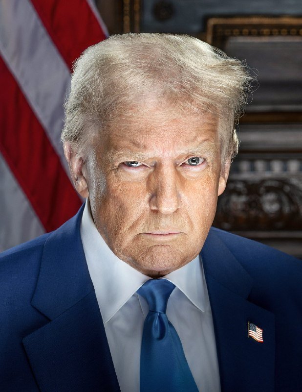 An older man with blond hair in a blue suit and tie stares at the camera with a serious expression, with an American flag visible in the background.
