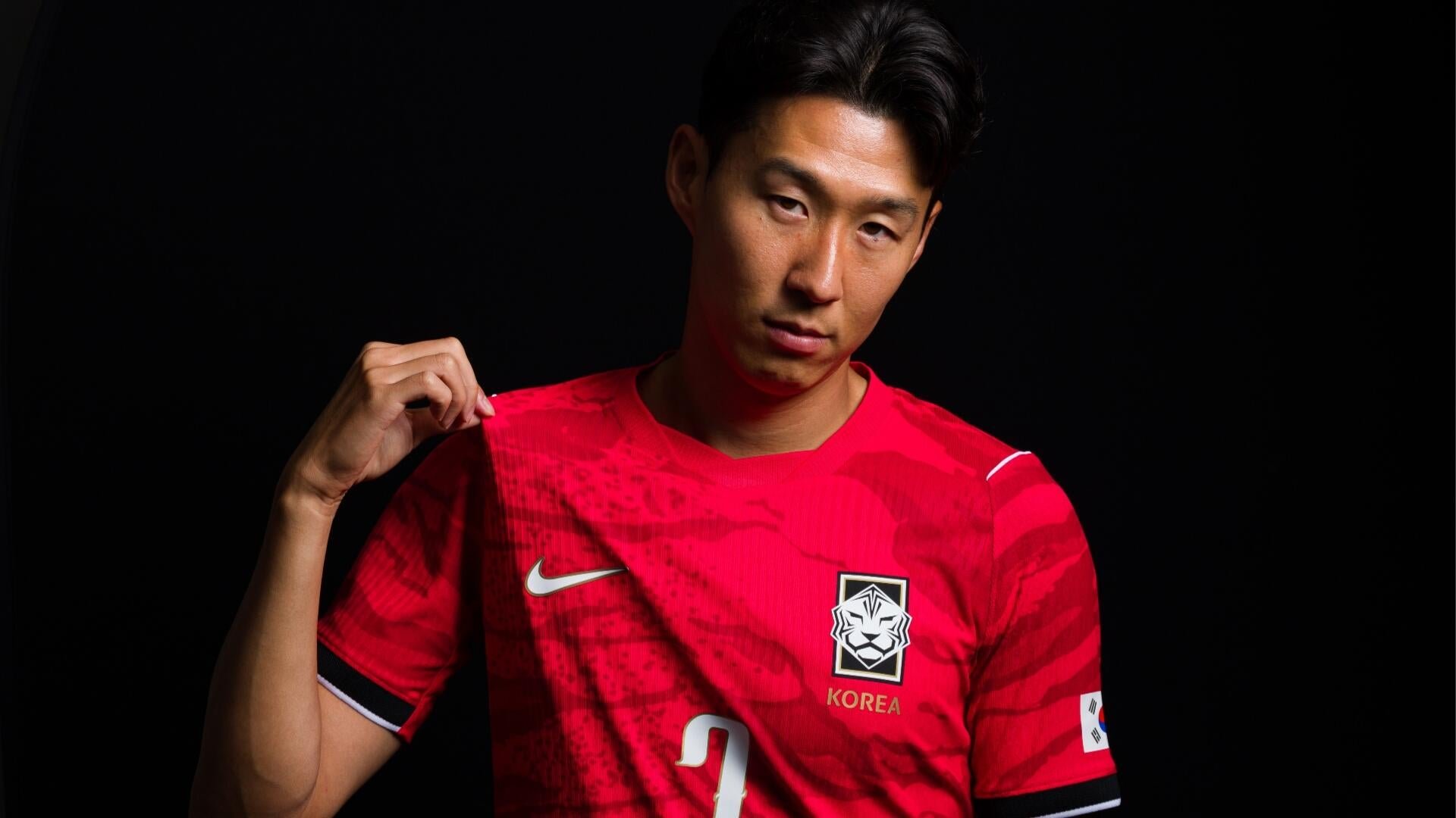 A man poses against a black background wearing a red South Korea national football jersey featuring a tiger crest, "KOREA" text, Nike logo, and the number 3.