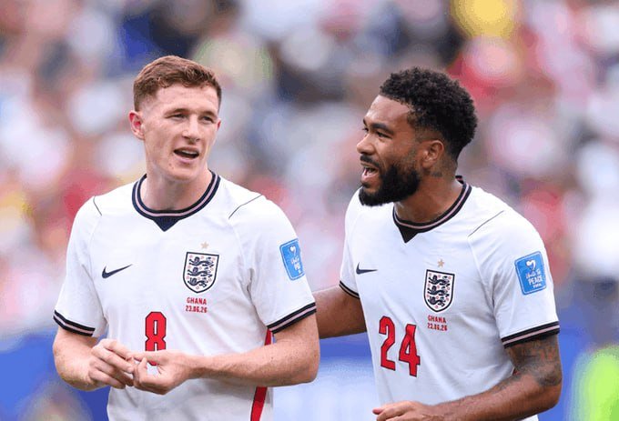 Two soccer players in white England jerseys with red numbers 8 and 24 celebrate together, one shouting with a clenched fist, during a match in a crowded stadium.
