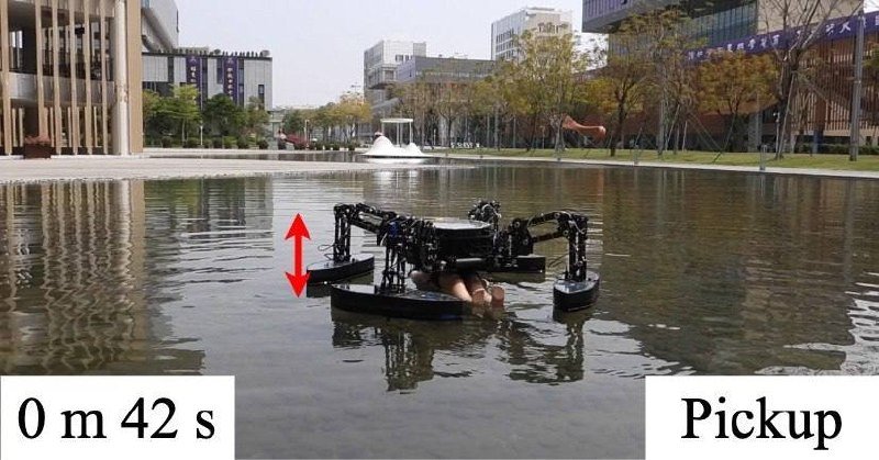A multi-rotor aquatic robot floats on a reflecting pond in an urban plaza, grasping an object; text reads "0 m 42 s" and "Pickup" with a red vertical arrow.