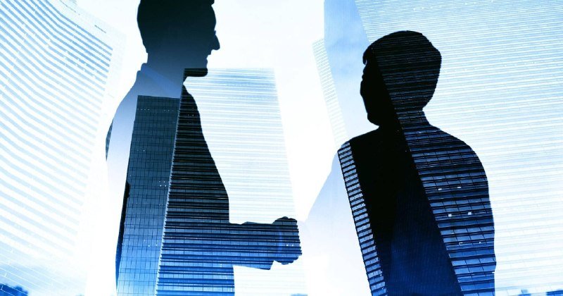 Silhouettes of two businessmen shaking hands against a backdrop of towering glass skyscrapers.