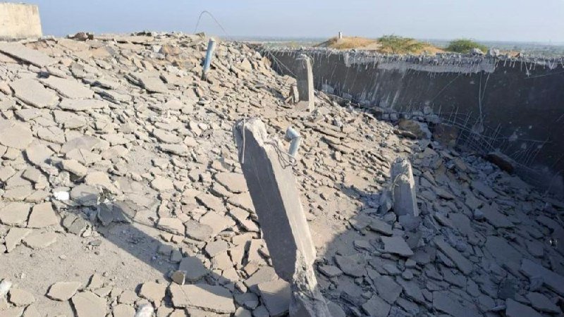 Concrete debris and exposed rebar litter a damaged rooftop overlooking a hazy landscape.