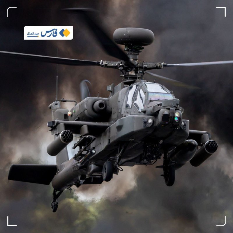 A dark military attack helicopter with a domed radar hovers in flight against a blurred smoky backdrop, with a small logo visible in the upper left corner.