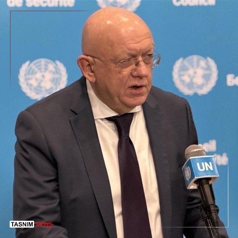 A bald man in a dark suit and tie speaks into a UN-branded microphone against a blue United Nations backdrop.
