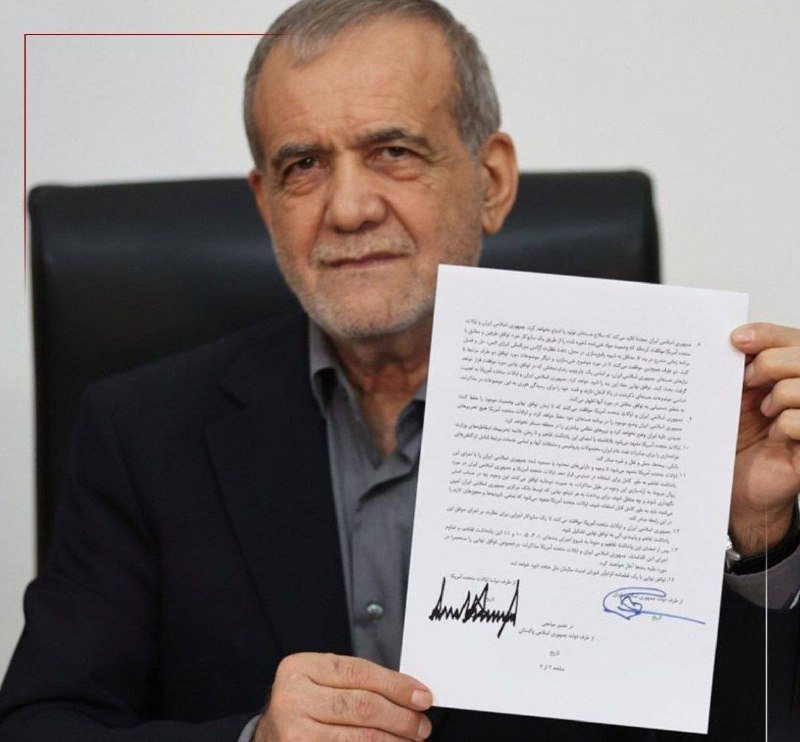 A gray-haired, bearded man in a dark suit holds up a printed document containing Persian script and two signatures, looking directly at the camera.