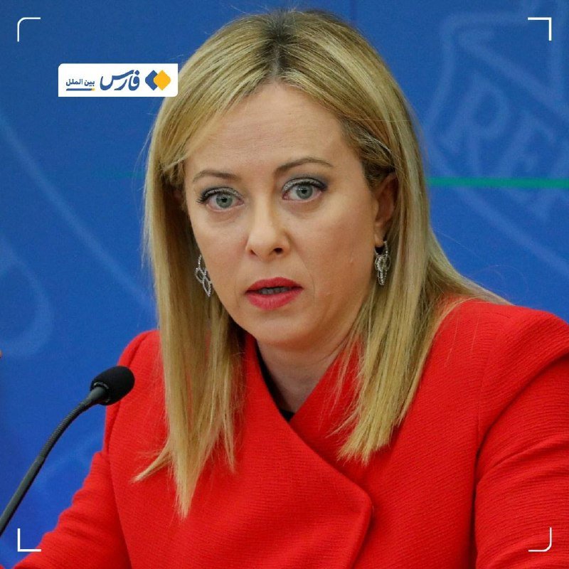 A blonde woman in a red jacket speaks into a microphone at a press briefing, with a Persian/Farsi logo visible in the upper left corner.