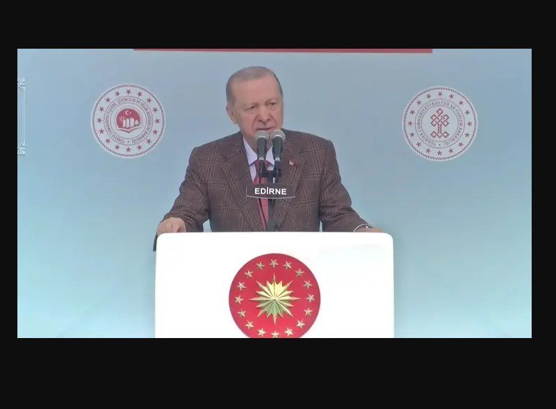 A man in a checked suit speaks at a podium labeled "EDIRNE," with Turkish government and presidency emblems displayed on the backdrop.