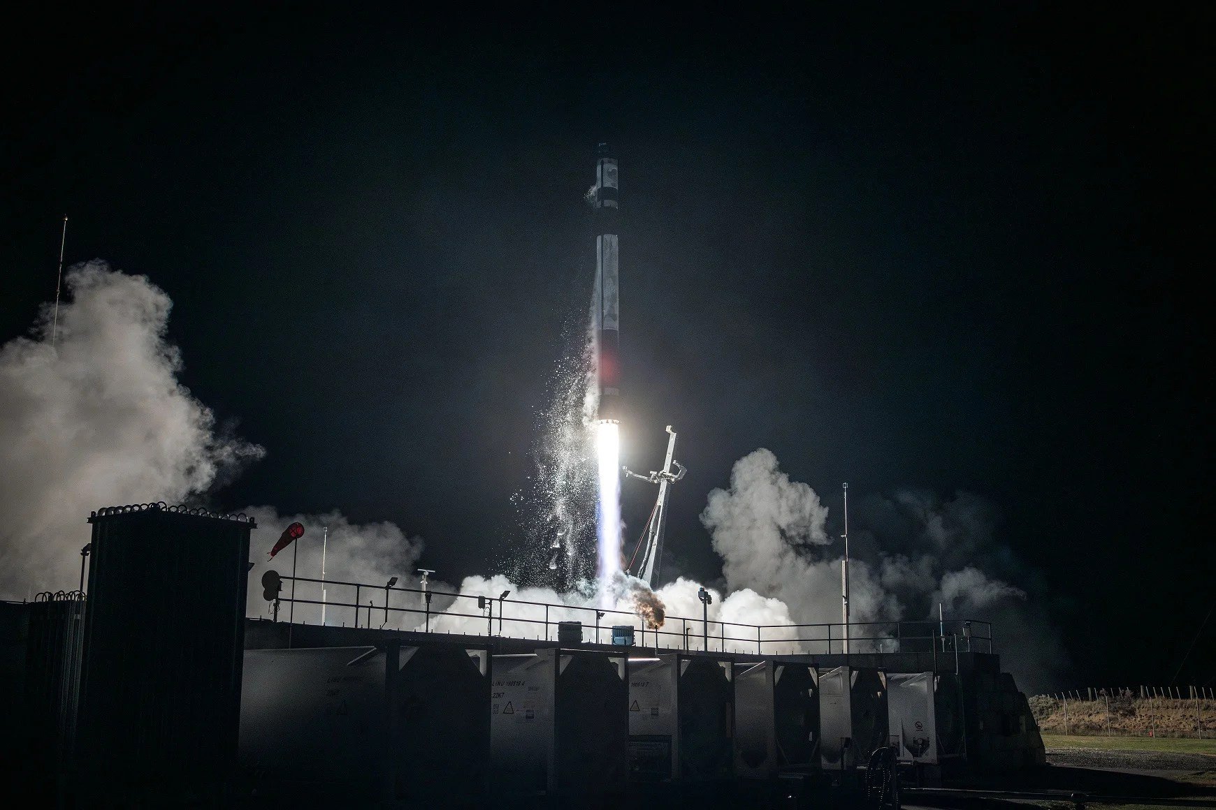A rocket lifts off at night from a launch pad, its engine producing a bright flame and billowing clouds of white smoke and steam.