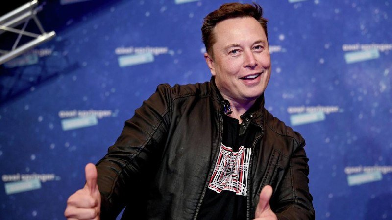A smiling man in a black leather jacket gives two thumbs up in front of a blue backdrop with partially legible text.