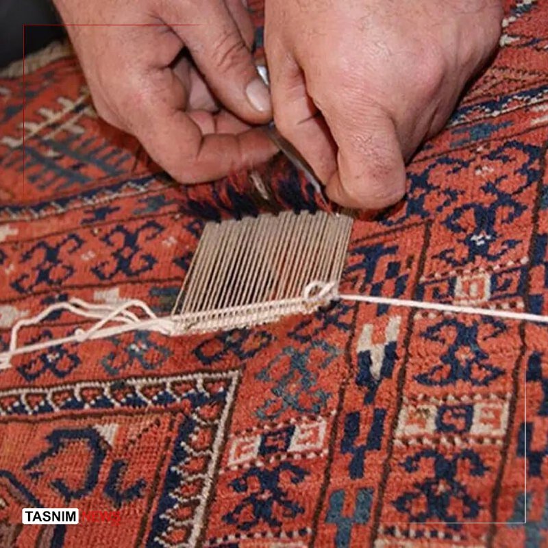 Close-up of hands using a small tool to tie knots on a loom, weaving an intricate red and navy patterned rug.