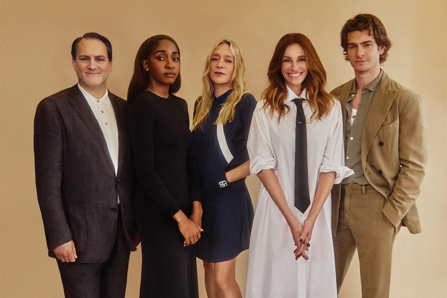 Five people pose together against a beige backdrop, smiling at the camera in formal and semi-formal attire.