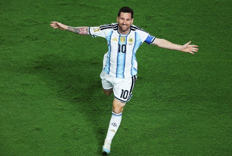 A bearded soccer player wearing a light blue and white striped jersey with the number 10 runs across a green field with arms outstretched and a smile.
