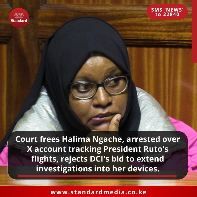 A woman wearing a black hijab and glasses sits with her hand near her chin in a wood-paneled room, with news graphics overlaid on the image.
