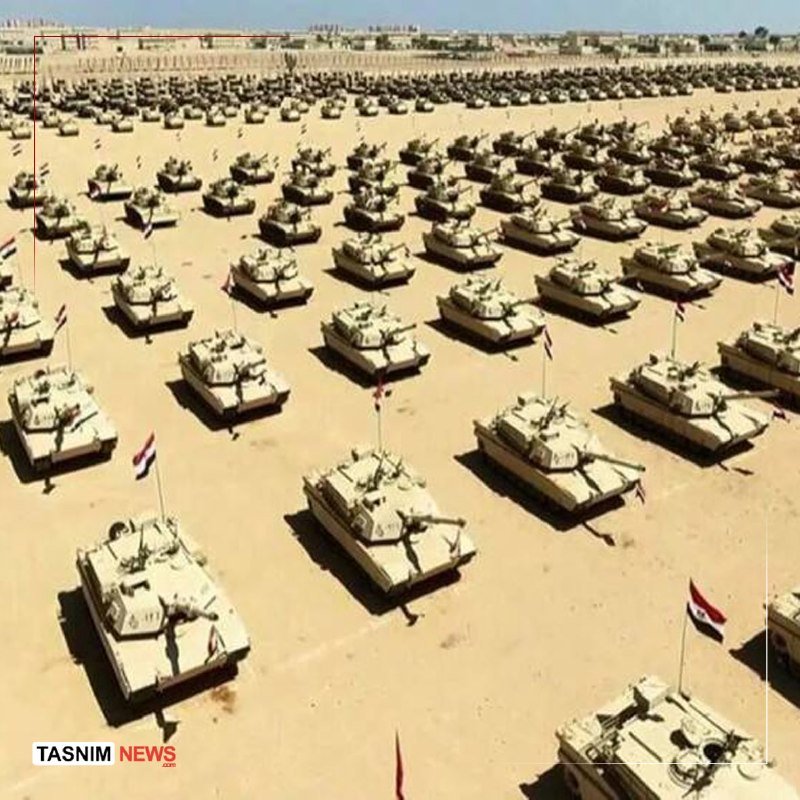 Hundreds of tan-colored tanks are arranged in neat rows across a vast desert landscape, each flying a small flag, with a "TASNIM NEWS" watermark in the corner.