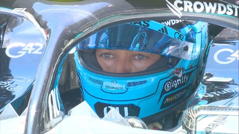 A driver wearing a blue helmet with "Crowdstrike," "G42," and "Signify" sponsor logos sits inside a race car cockpit, looking forward.