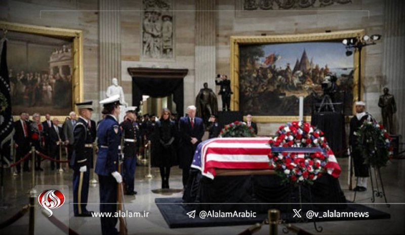 An American flag-draped casket lies in state inside the U.S. Capitol Rotunda, with uniformed military honor guards standing watch as mourners in dark attire gather nearby.