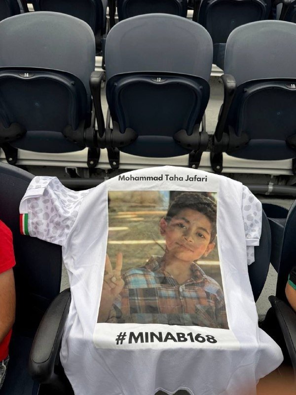 A white jersey bearing the name "Mohammad Taha Jafari," a photograph of a young boy making a peace sign, and the hashtag "#MINAB168" is draped over stadium seating.