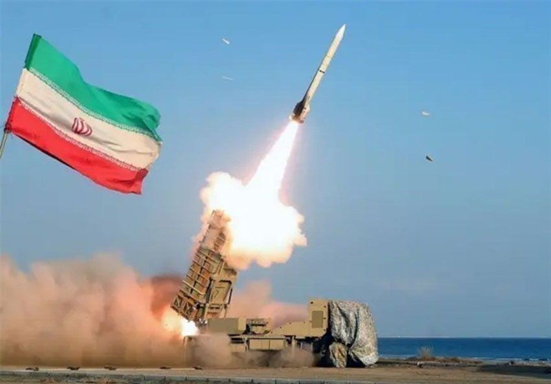A missile launches skyward from a mobile launcher near a coastline, with an Iranian flag waving in the foreground and dust billowing from the ignition.