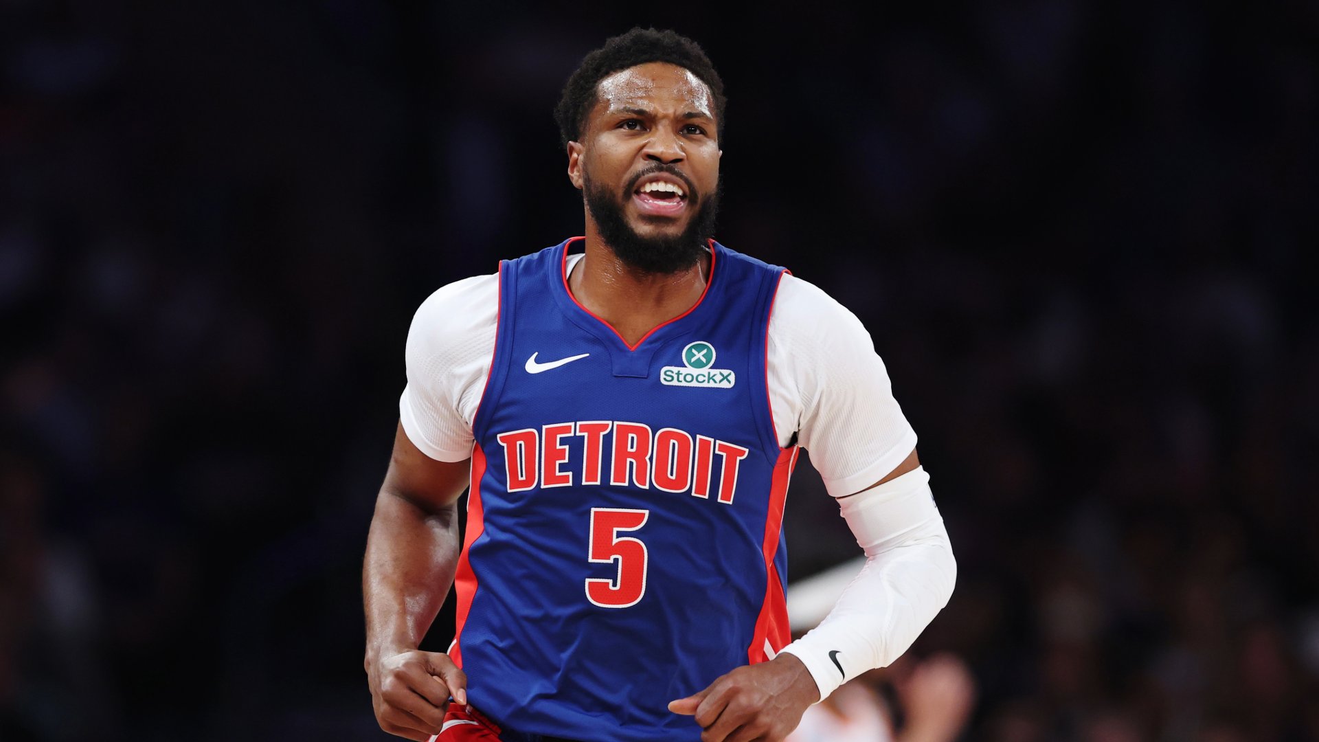 A bearded basketball player in a blue Detroit jersey numbered 5 reacts with an open-mouthed expression during a game.