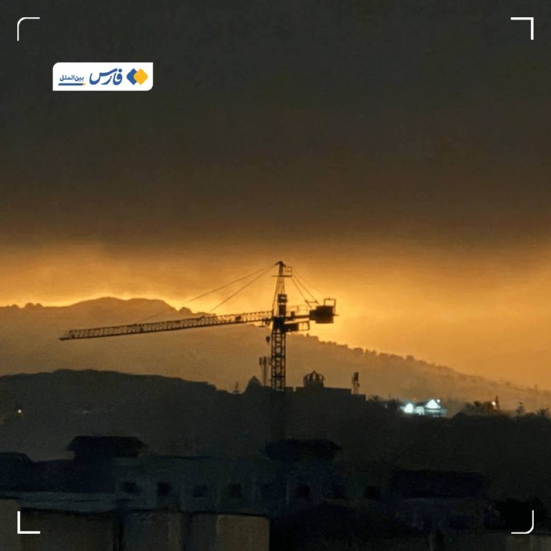 A silhouetted construction crane stands against an orange sunset sky above distant mountain ridges and darkened rooftops.