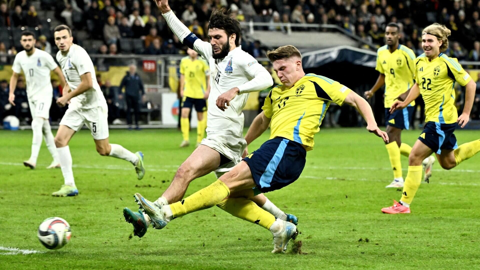 A player in a yellow jersey strikes the ball while a white-jerseyed opponent challenges him during a soccer match in a crowded stadium.
