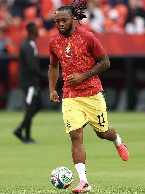 A soccer player wearing a red jersey with the number 11 and yellow shorts dribbles a ball on a green field.