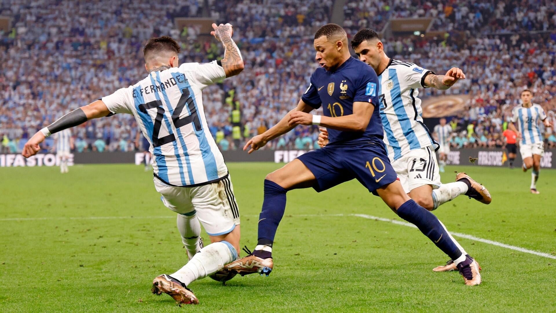 A soccer player in a dark blue jersey with the number 10 dribbles the ball while being challenged by two opponents in light blue and white striped jerseys during a stadium match.