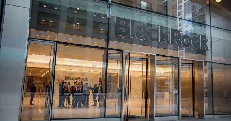People gather inside the glass-walled lobby of a building featuring a large "BlackRock" sign above the entrance.